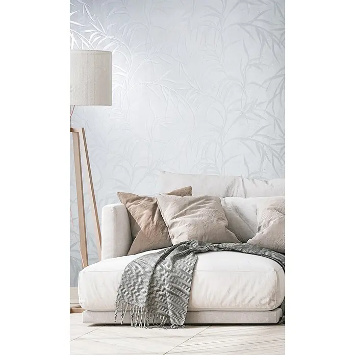 Marburg City Glow Vliestapete Uni II - Weiß, Uni, 10,05 x 0,53 m - Hellgraue Tapete mit dezentem botanischem Muster in einem Wohnzimmer mit Sofa und Stehlampe.