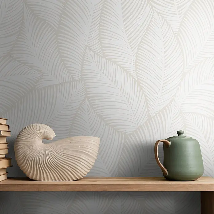 Marburg Novamur Plus Fresh UP Vliestapete Flora VII - Weiß-Beige, Floral, 10,05 x 0,53 m - Eine beige Muschelskulptur, Bücher und eine grüne Teekanne auf einem Holzregal vor einer Palmblatt-Tapete.
