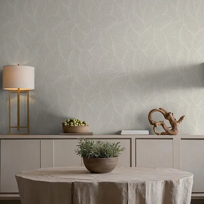 Marburg Novamur Plus Fresh UP Vliestapete Flora VII - Beige, Floral, 10,05 x 0,53 m - Hellgraue Tapete mit dezentem Muster aus stilisierten helleren grauen Blättern, an einer Wand in einem modernen Raum.