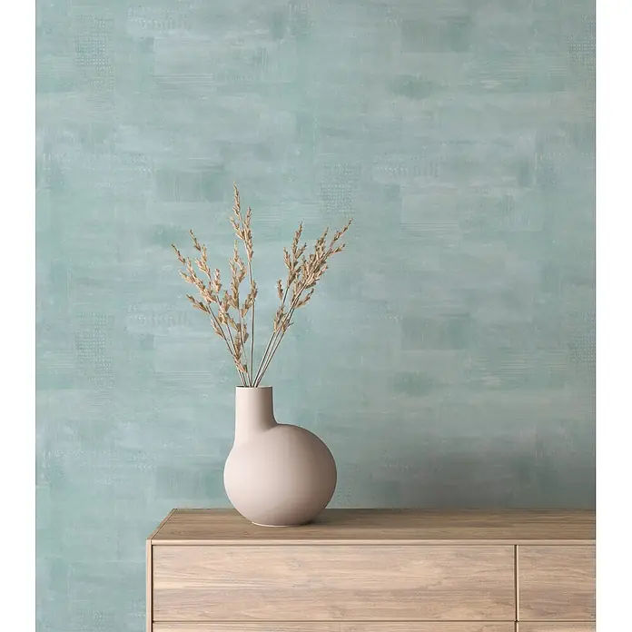 Marburg Novamur Plus Fresh UP Vliestapete Uni I - Grün-Blau, Uni, 10,05 x 0,53 m - Eine matte beigefarbene Vase mit getrockneten Gräsern auf einem hellen Holzschrank vor einer texturierten türkisblauen Wand.