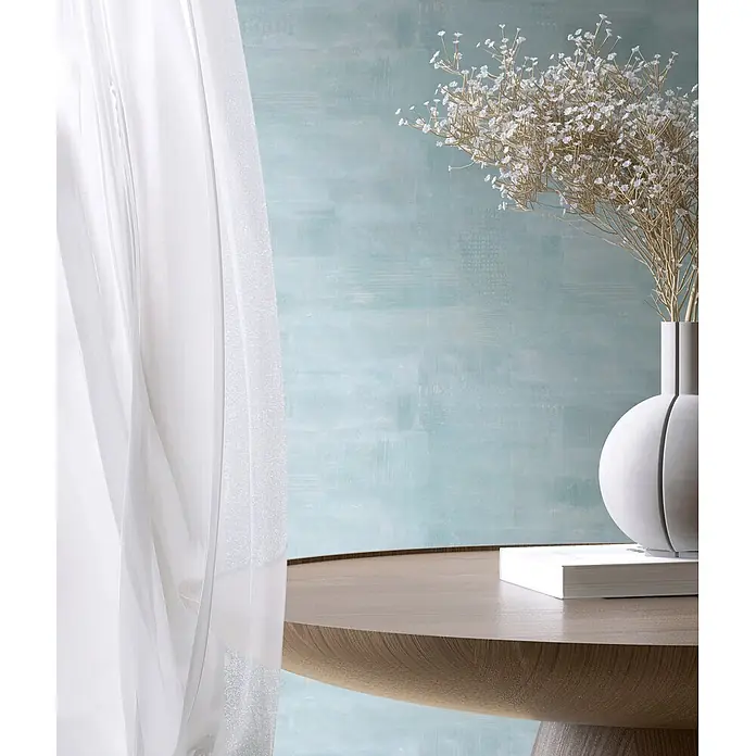 Marburg Novamur Plus Fresh UP Vliestapete Uni I - Blau, Uni, 10,05 x 0,53 m - Weiße Vase mit goldenen Trockenblumen auf einem Holztisch, neben transparenten Vorhängen vor einer blauen Wand.