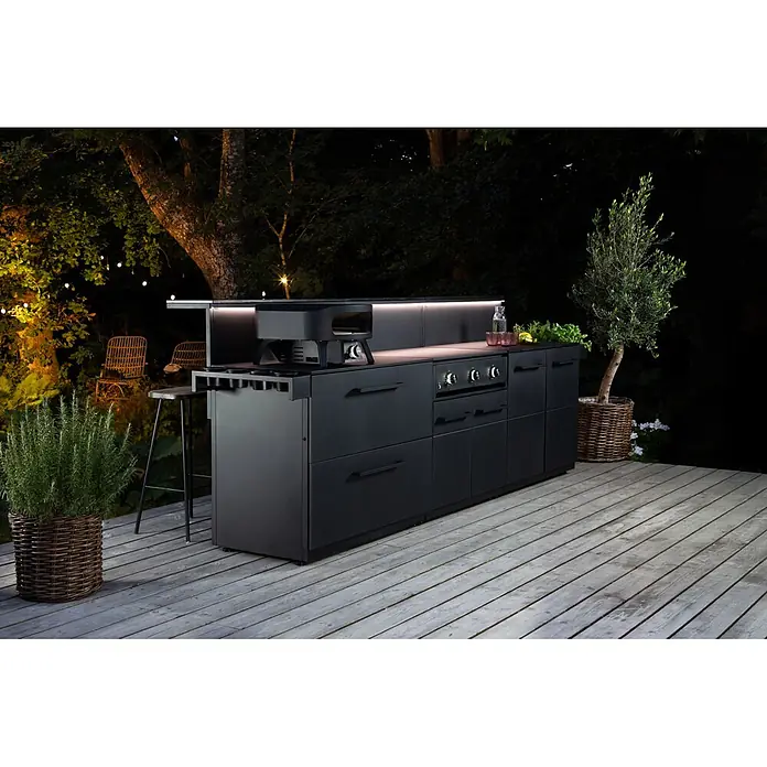 Cozze Toppingstation - Stahl, B x T x H: 60 x 13 x 10 cm - Schwarze Outdoor-Küche mit integriertem Pizzaofen, Kochfeld und Bar auf Holzterrasse bei Nacht.