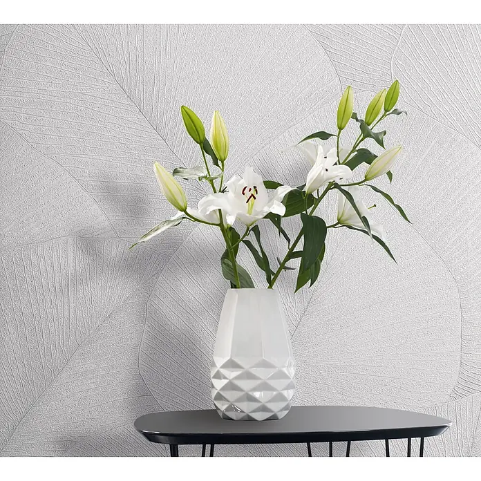 Marburg Kumano Vliestapete Floral - Weiß, Floral, 10,05 x 0,53 m - Weiße, geometrisch gemusterte Vase mit weißen Lilien auf einem dunkelgrauen Beistelltisch.