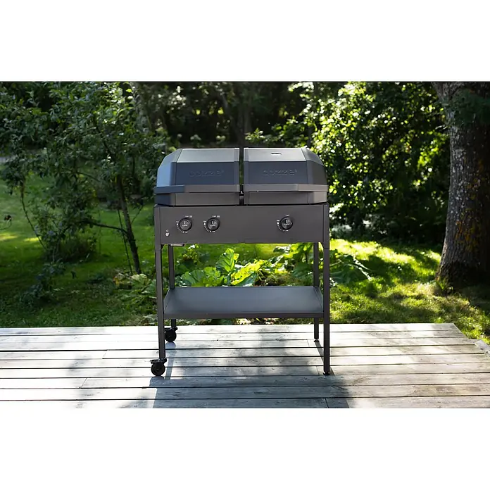 Cozze Hybrid-Grill Quattro 900 - Grillfläche (B x T): 72,7 x 34,5 cm, 13 kW, Anzahl Brenner: 3 Stk. - Dunkelgrauer Cozze Gasgrill mit zwei Brennern auf Rollen, steht auf einer Holzterrasse im Freien.
