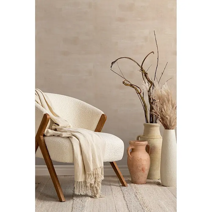 Marburg Novamur Plus Fresh UP Vliestapete Uni - Beige-Braun, Uni, 10,05 x 0,53 m - Ein cremefarbener Bouclé-Sessel mit Holzrahmen und beigem Überwurf in einem gemütlichen Wohnraum.
