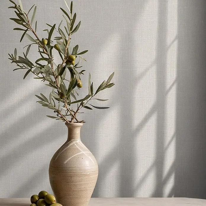 Marburg Boho Vliestapete Uni - Braun, Uni, 10,05 x 0,53 m - Ein Olivenzweig mit grünen Oliven und Blättern in einer beigen Keramikvase, auf einer hellen Oberfläche.