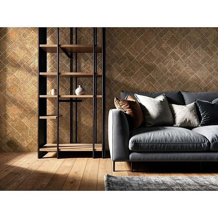 Marburg Ritus Vliestapete Grafik I - Gold, Grafisch, 10,05 x 0,53 m - Ein gemütliches graues Polstersofa mit Plüschkissen steht neben einem eleganten Regal aus schwarzem Metall und Holz vor einer strukturierten Goldwand.