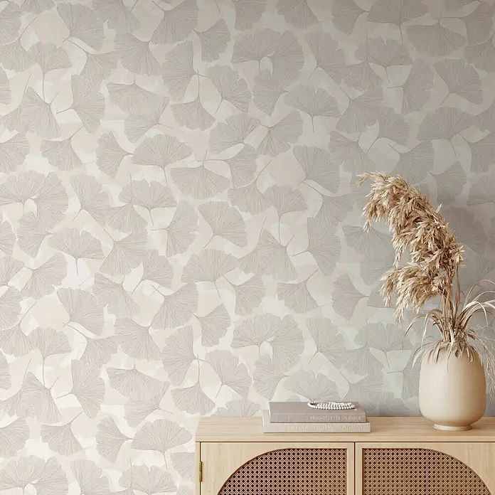 Marburg Boho Vliestapete Floral - Grau-Beige, Floral, 10,05 x 0,53 m - Tapete mit neutralem Ginkgoblatttmuster an einer Wand über einem hellen Holzschrank mit getrocknetem Pampasgras und Büchern.