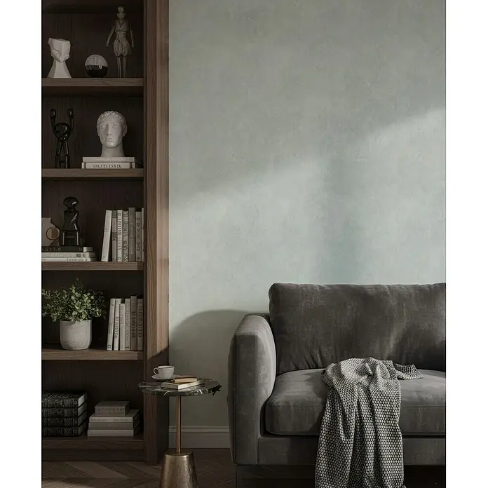 Marburg Whisper Vliestapete Putzoptik I - Grün, Sonstiges, 10,05 x 0,53 m - Dunkelgraues Polstersofa mit gemusterter Decke in einem modernen Wohnzimmer neben einem Holzregal.