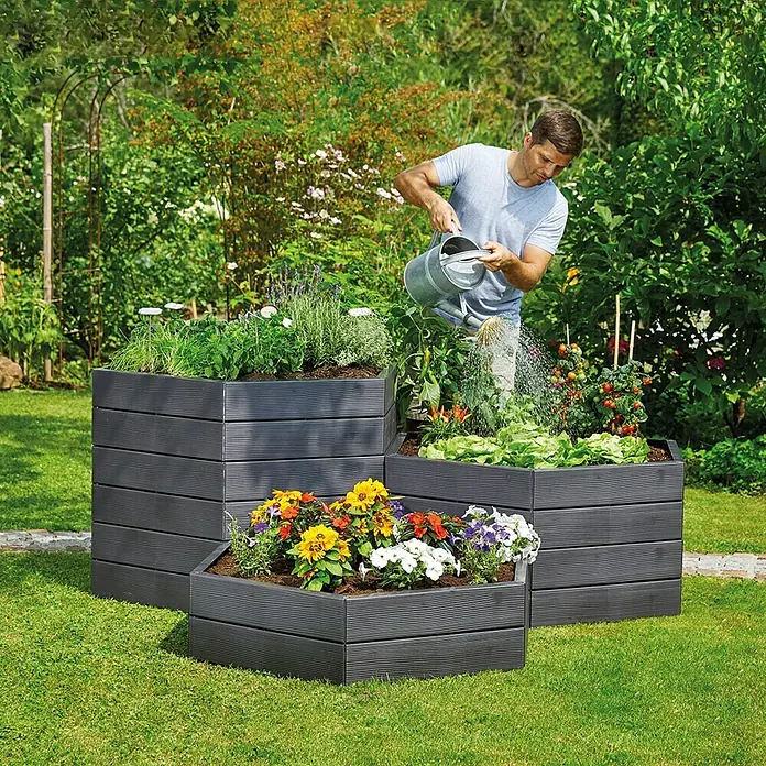 Garantia Hochbeet Ergo Wood - Ø x H: 110 x 25 cm, Kunststoff, Anthrazit - Mann gießt Pflanzen in einem erhöhten, mehrstöckigen, grauen Pflanzgefäß im Garten.