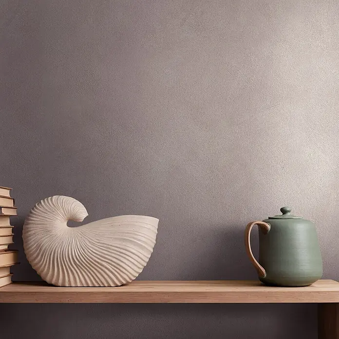 Marburg Whisper Vliestapete Putzoptik I - Lehmbraun, Sonstiges, 10,05 x 0,53 m - Dekorative Muschelskulptur, Bücherstapel und grüne Keramikkanne mit Holzgriff auf einem hellen Holzregal.