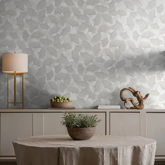 Marburg Boho Vliestapete Floral - Grau-Weiß, Floral, 10,05 x 0,53 m - Hellgraue Tapete mit Ginkgo-Blattmuster schmückt eine Wand in einem modernen Wohnraum.