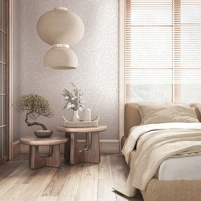 Marburg Boho Vliestapete Floral I - Weiß-Grau, Floral, 10,05 x 0,53 m - Ein gemütliches Schlafzimmer mit Bett, zwei runden Holztischen und geflochtenen Laternen vor einer Wand mit Blattmuster.