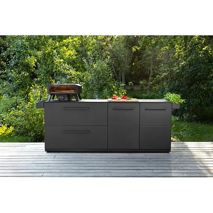Cozze Elements Outdoorküchen-Modul Schubladenschrank - Schwarz, B x T x H: 110 x 60 x 88,5 cm, Stahl - Dunkelgraue Outdoor-Küchenzeile mit Pizzaofen, der eine Pizza backt. Zutaten liegen auf der hellen Arbeitsplatte.
