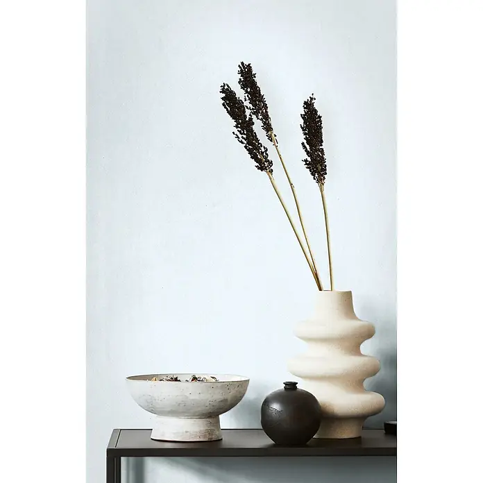 Marburg Vliestapete Novamur Oriana Uni - Blau, Uni, 10,05 x 0,53 m - Heimdeko: gewellte beige Vase mit Trockenpflanzen, weiße Keramik-Potpourri-Schale und kleine schwarze Vase auf einem dunklen Regal.