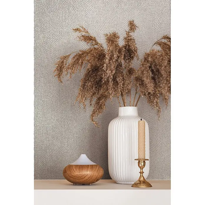 Marburg Whisper Vliestapete Putzoptik II - Creme, Sonstiges, 10,05 x 0,53 m - Eine weiße gerippte Vase mit getrocknetem Pampasgras, ein Holz-Diffusor und eine Bienenwachskerze in einem Messinghalter, auf einem Regal arrangiert.