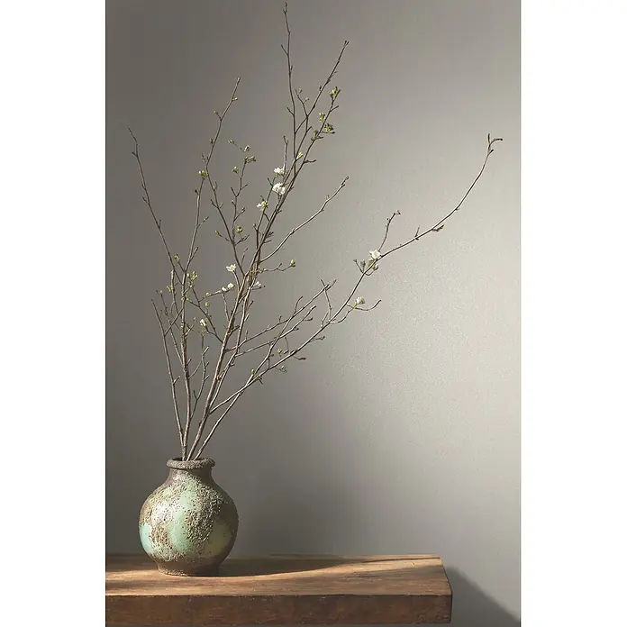 Marburg Vliestapete Novamur Naomi Uni I - Weiß-Beige, Uni, 10,05 x 0,53 m - Grüne, texturierte Vase mit zarten, blühenden Zweigen auf einem rustikalen Holztisch.