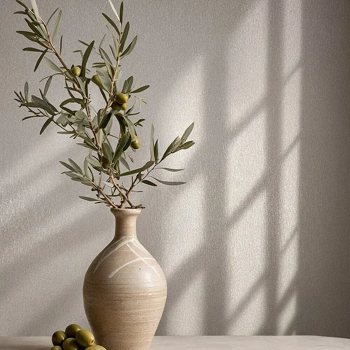 Marburg Vliestapete Novamur Naomi Uni II - Beige-Grau, Uni, 10,05 x 0,53 m - Ein dekorativer Olivenzweig mit grünen Oliven in einer beigen Keramikvase, mit zusätzlichen Oliven auf dem Tisch.