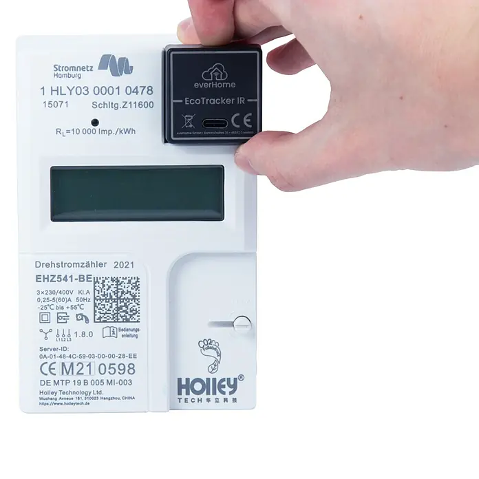 EverHome Energiekosten-Messgerät EcoTracker IR - Schwarz - Eine Hand hält einen schwarzen Smart-Meter-Leser, der an einem weißen Stromzähler befestigt ist.