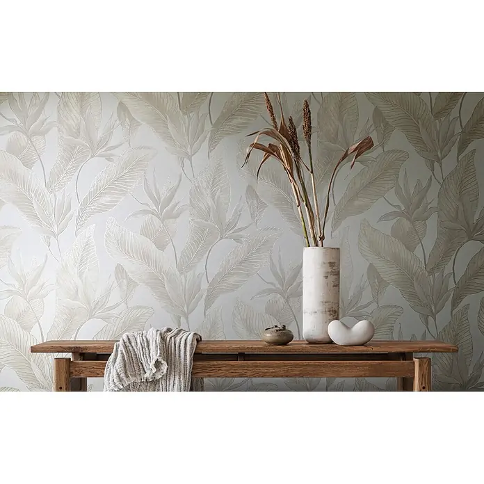 Marburg Whisper Vliestapete Floral - Beige, Floral, 10,05 x 0,53 m - Elegante Tapete mit zartem hellbeigem Tropenblatt- und Blütenmuster, an einer Wand hinter einer Holzbank gezeigt.