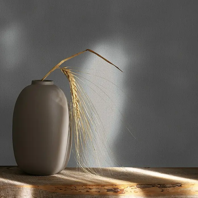 Marburg Whisper Vliestapete Uni - Grau, Uni, 10,05 x 0,53 m - Braune Vase mit getrockneten goldenen Weizenähren auf einem Holzuntergrund, von natürlichem Licht und Schatten beschienen.
