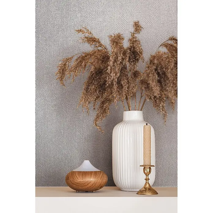 Marburg Whisper Vliestapete Putzoptik II - Beige-Grau, Sonstiges, 10,05 x 0,53 m - Ein Diffusor in Holzoptik, weiße Vase mit getrocknetem Pampasgras und eine beigefarbene Kerze in einem Messinghalter auf einem Regal.