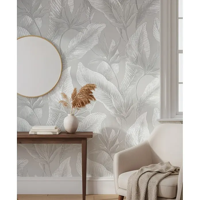Marburg Whisper Vliestapete Floral - Grau, Floral, 10,05 x 0,53 m - Botanische Tapete mit grauen und silbernen Blättern schmückt eine Wand in einem hellen Raum, ergänzt durch Konsole und Sessel.