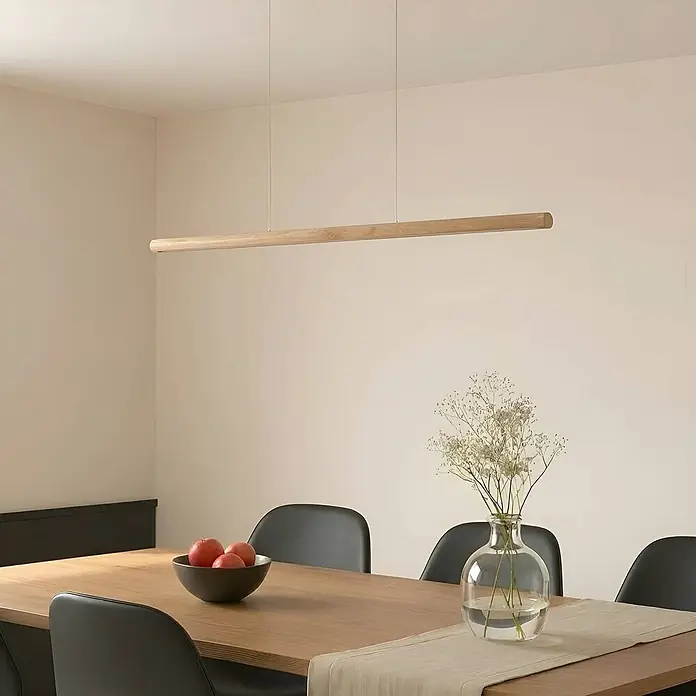 Lucande Pendelleuchte Maruta - L x B x H: 120 x 7 x 3,3 cm, Holz hell, helles Holz - Eine lange, lineare Pendelleuchte aus Holz hängt über einem Esstisch und sorgt für Umgebungsbeleuchtung.