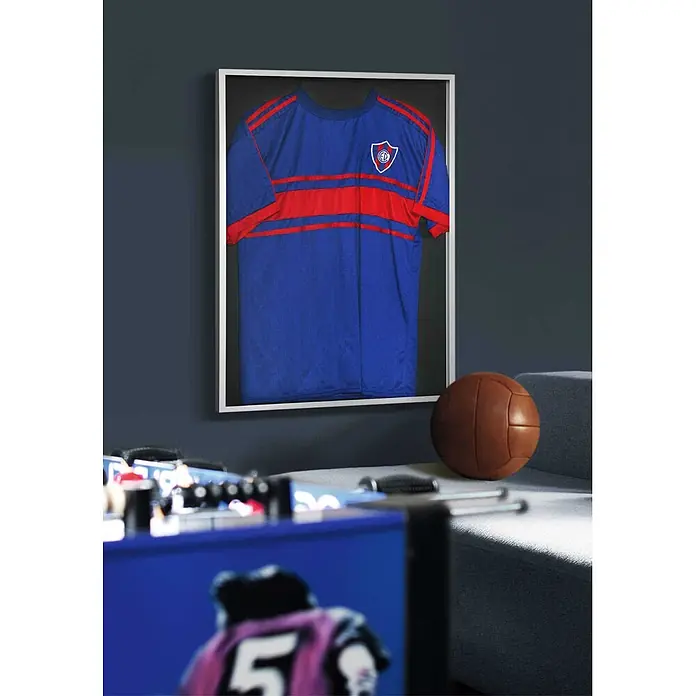 Nielsen Alurahmen Frame Box 2 - 60 x 80 cm, Schwarz - Gerahmtes blau-rotes Sporttrikot mit Wappen, an einer Wand in einem Raum mit Vintage-Fußball und Kicker.