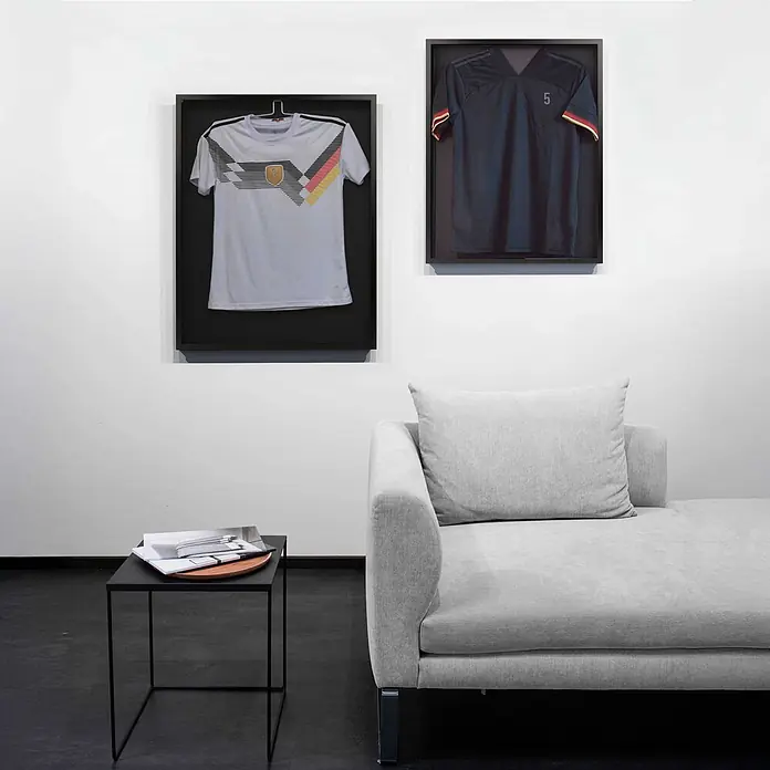 Nielsen Alurahmen Frame Box 2 - 60 x 80 cm, Schwarz - Zwei gerahmte Fußballtrikots (weiß und dunkelblau) an einer weißen Wand in einem modernen Raum mit grauem Sofa und schwarzem Beistelltisch.