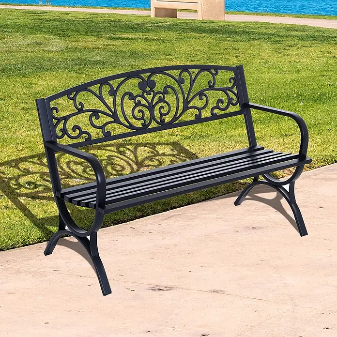 Outsunny Gartenbank - Metall, Schwarz - Schwarze Metall-Gartenbank mit verziertem Rückenteil, auf einem gepflasterten Weg in einer Parkanlage am Wasser.