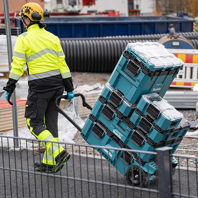 Makita Werkzeugkasten Maktrak Trolley L - Kunststoff, L x B x H: 101,1 x 56,5 x 29,5 cm - Türkis-schwarze Makita Werkzeugkisten auf einem Rollwagen, von Bauarbeiter in Warnkleidung geschoben.
