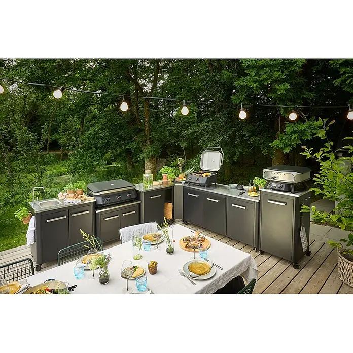 Cozze Outdoorküchen-Modul niedrig - Schwarz/Silber, B x T x H: 93,5 x 67 x 70 cm - Dunkelgraue modulare Außenküche mit Edelstahl-Arbeitsplatten, Grill, Spüle und Pizzaofen auf einer Terrasse für ein Essen im Freien.