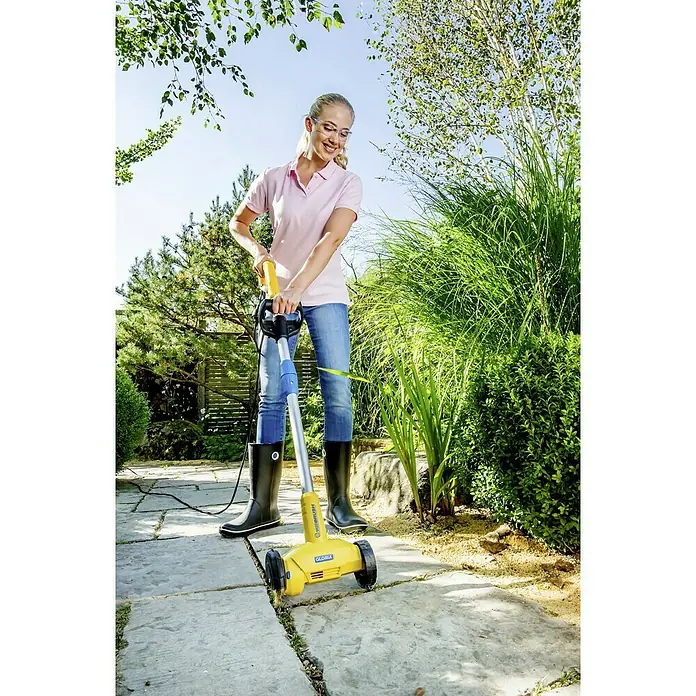 Gloria WeedBrush Fugenreiniger300 W, 1.800 U/min - Eine Frau benutzt eine Gloria WeedBrush zur Reinigung von Pflastersteinen im Garten, umweltfreundlich und effizient.