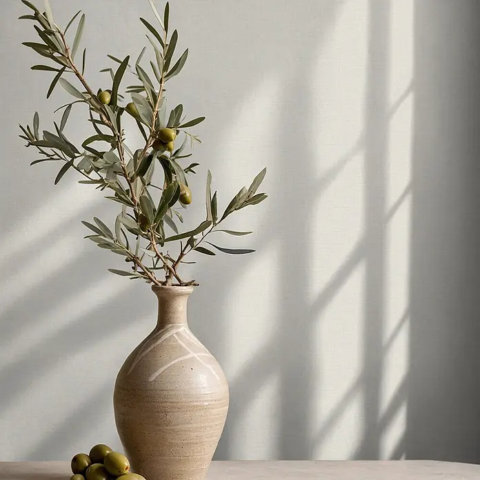 Marburg Vliestapete Novamur Oriana - Beige, Uni, 10,05 x 0,53 m - Rustikale Keramikvase mit Olivenzweigen und grünen Oliven auf einem Tisch, mit Fensterschatten an einer strukturierten Wand.