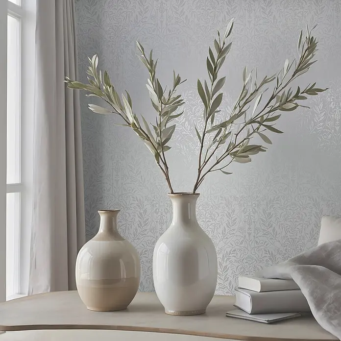 Marburg Vliestapete Novamur Oriana Floral I - Weiß, Floral, 10,05 x 0,53 m - Zwei Keramikvasen, eine weiß und eine zweifarbig, mit Olivenzweigen auf einem hellen Tisch arrangiert.