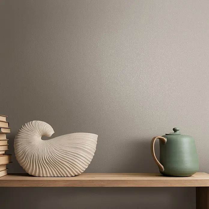 Marburg Vliestapete Novamur Naomi Uni I - Grau-Beige, Uni, 10,05 x 0,53 m - Dekoratives Holzregal mit Büchern, einer großen weißen Muschelskulptur und einer grünen Keramikkanne.