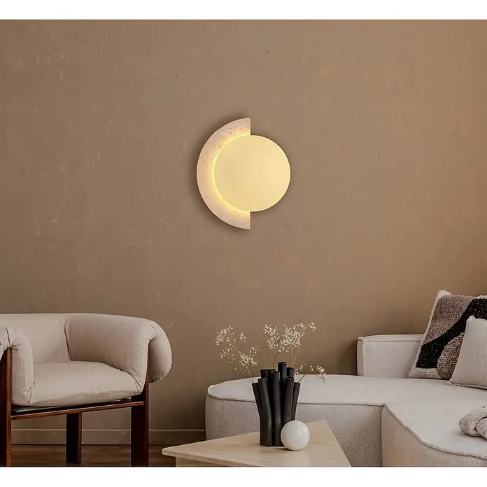 Globo LED-Wandleuchte Rojas - 14 W, Warmweiß - Runde Wandleuchte mit strukturiertem Halbkreisrahmen, spendet warmes Licht an einer braunen Wand in einem Wohnzimmer.