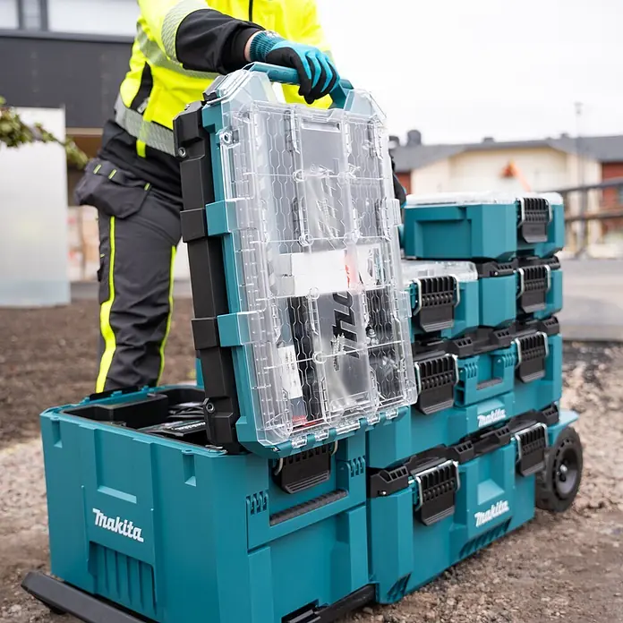 Makita Organizer Maktrak Flach L - L x B x H: 59,6 x 38,7 x 8,5 cm, Anzahl Fächer: 11 Stk. - Arbeiter handhabt türkisfarbenes Makita Modul-Werkzeugkastensystem mit Klarsichtdeckeln, gestapelt auf einer rollenden Basis auf Baustelle.