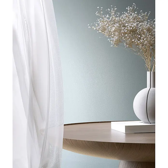 Marburg Vliestapete Novamur Naomi Uni I - Blau, Uni, 10,05 x 0,53 m - Runder Holztisch mit weißer Vase, Trockenblumen und Buch, neben transparenten Vorhängen.