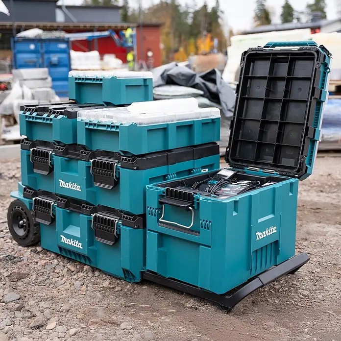 Makita Werkzeugkasten Maktrak XL - Kunststoff, L x B x H: 56,5 x 39,4 x 40,2 cm - Gestapelte türkisfarbene Makita Werkzeugkoffer auf einem Rollwagen auf einer Baustelle, einer offen mit Werkzeugen.