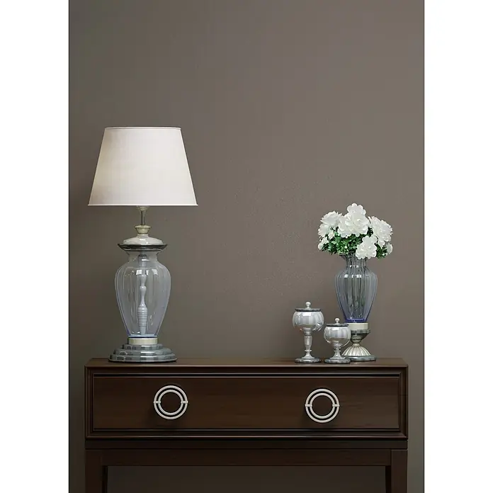 Marburg Vliestapete Novamur Naomi Uni I - Grau-Braun, Uni, 10,05 x 0,53 m - Dunkelbraune Holzkommode mit zwei Schubladen und weißen Griffen, darauf eine Lampe und Dekoartikel.