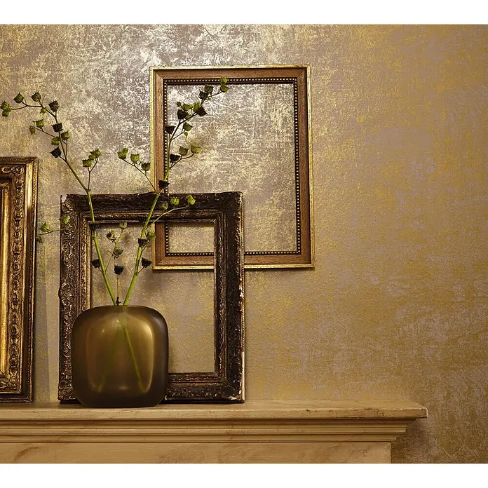 Marburg La Veneziana II Vliestapete - Gold, Uni, 10,05 x 0,53 m - Goldstrukturierte Tapete mit einer patinierten Metallic-Oberfläche, gezeigt hinter antiken Bilderrahmen und einer Vase auf einem Kaminsims.