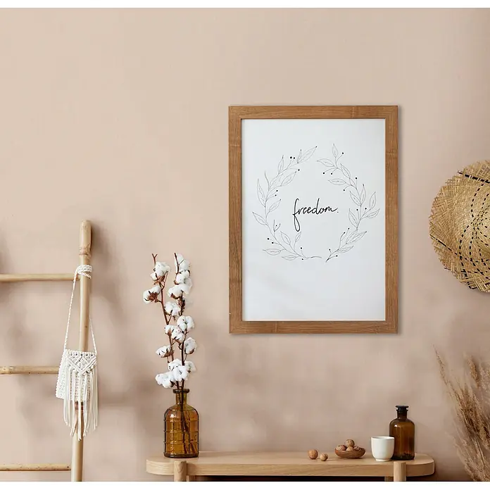Marburg Vliestapete Novamur Mona Uni - Beige, Uni, 10,05 x 0,53 m - Holzgerahmter Druck mit „freedom“-Text und Blattkranz, an beiger Wand in einem Raum im Boho-Stil.