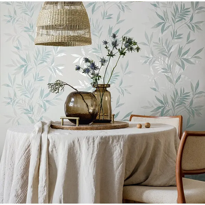 Marburg Vliestapete Novamur Mona Floral - Weiß-Grün, Floral, 10,05 x 0,53 m - Ein runder Tisch ist mit einer hellbeigen Leinentischdecke gedeckt, die ein entspanntes und elegantes Ambiente schafft.