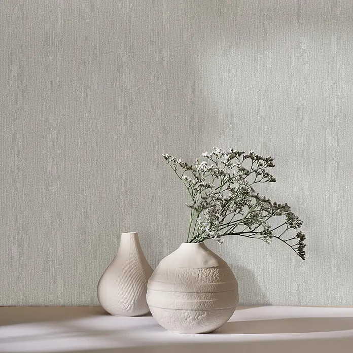 Marburg Vliestapete Novamur Mona Uni I - Beige, Uni, 10,05 x 0,53 m - Zwei dekorative cremefarbene Keramikvasen, eine gepunktet und die andere mit horizontalen Rillen, die zarte weiße Blumen halten.