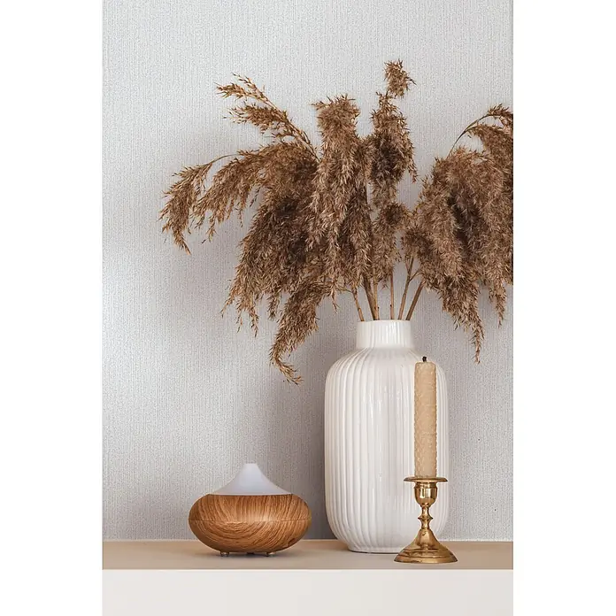 Marburg Vliestapete Novamur Mona Uni I - Weiß, Uni, 10,05 x 0,53 m - Ein Aroma-Diffusor in Holzoptik, eine weiße gerippte Vase mit Pampasgras und ein goldener Kerzenständer mit Kerze auf einem Regal.