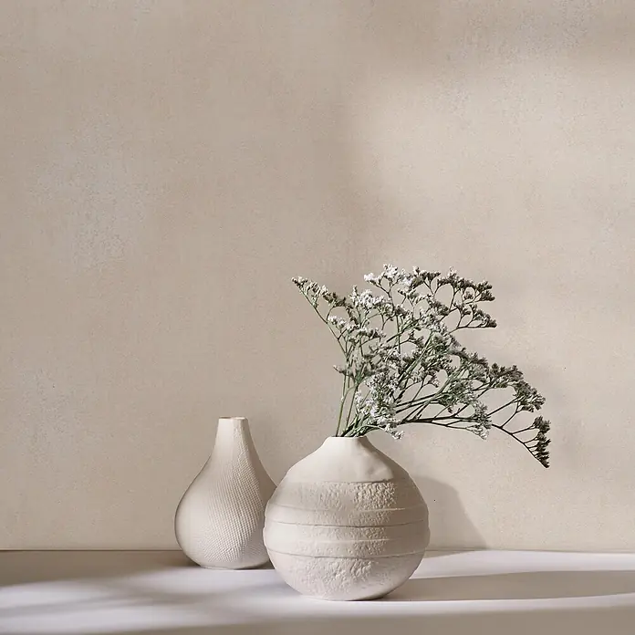 Marburg Vliestapete Novamur Leyla Betonoptik - Beige, Sonstiges, 10,05 x 0,53 m - Zwei texturierte beigefarbene Keramikvasen, eine mit getrockneten weißen Blumen, bilden ein ruhiges Arrangement.