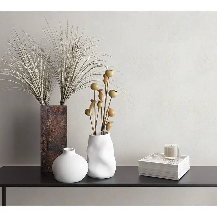 Marburg Vliestapete Novamur Leyla Betonoptik - Weiß, Sonstiges, 10,05 x 0,53 m - Dekoratives Arrangement auf dunklem Regal: hohe Vasen mit Trockengras und Holzstäbchen, eine kleine weiße Vase und Zeitschriften mit Kerze.