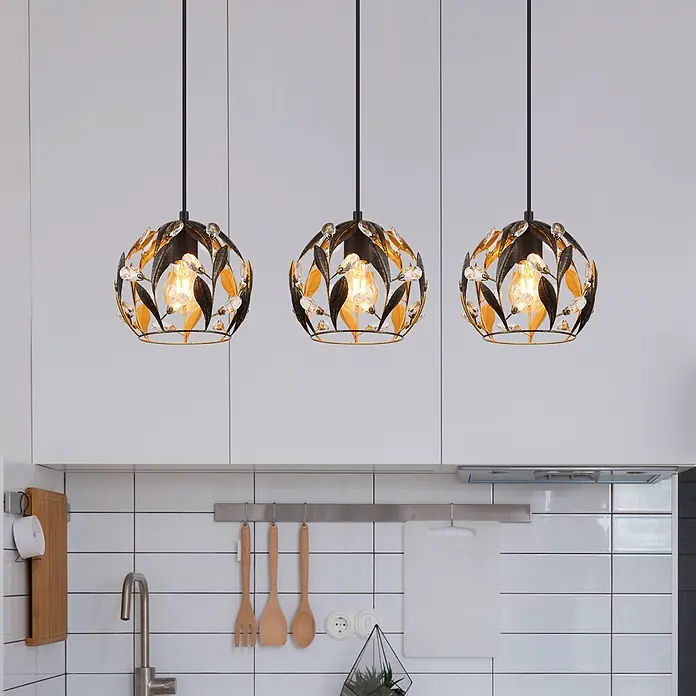 Globo Pendelleuchte Mika - 40 W, L x B x H: 740 x 200 x 1.500 mm, E27 - Drei schwarze und goldene Blatt-Design-Pendelleuchten mit Kristallakzenten und warmen Filamentlampen in einer modernen Küche.